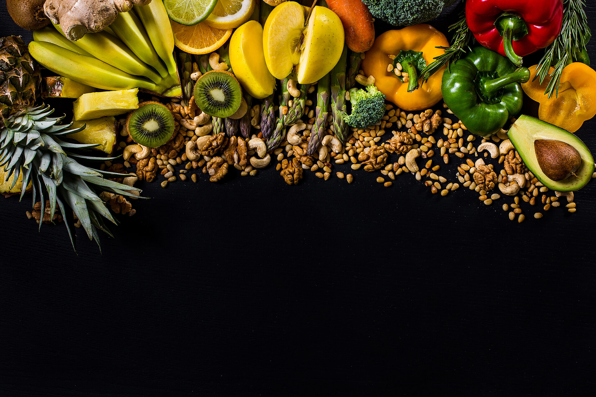 Black background with walnuts, cashews, pine nuts, paprika, carrots, broccoli, bananas, pineapples, citrus fruits, ginger and kiwi