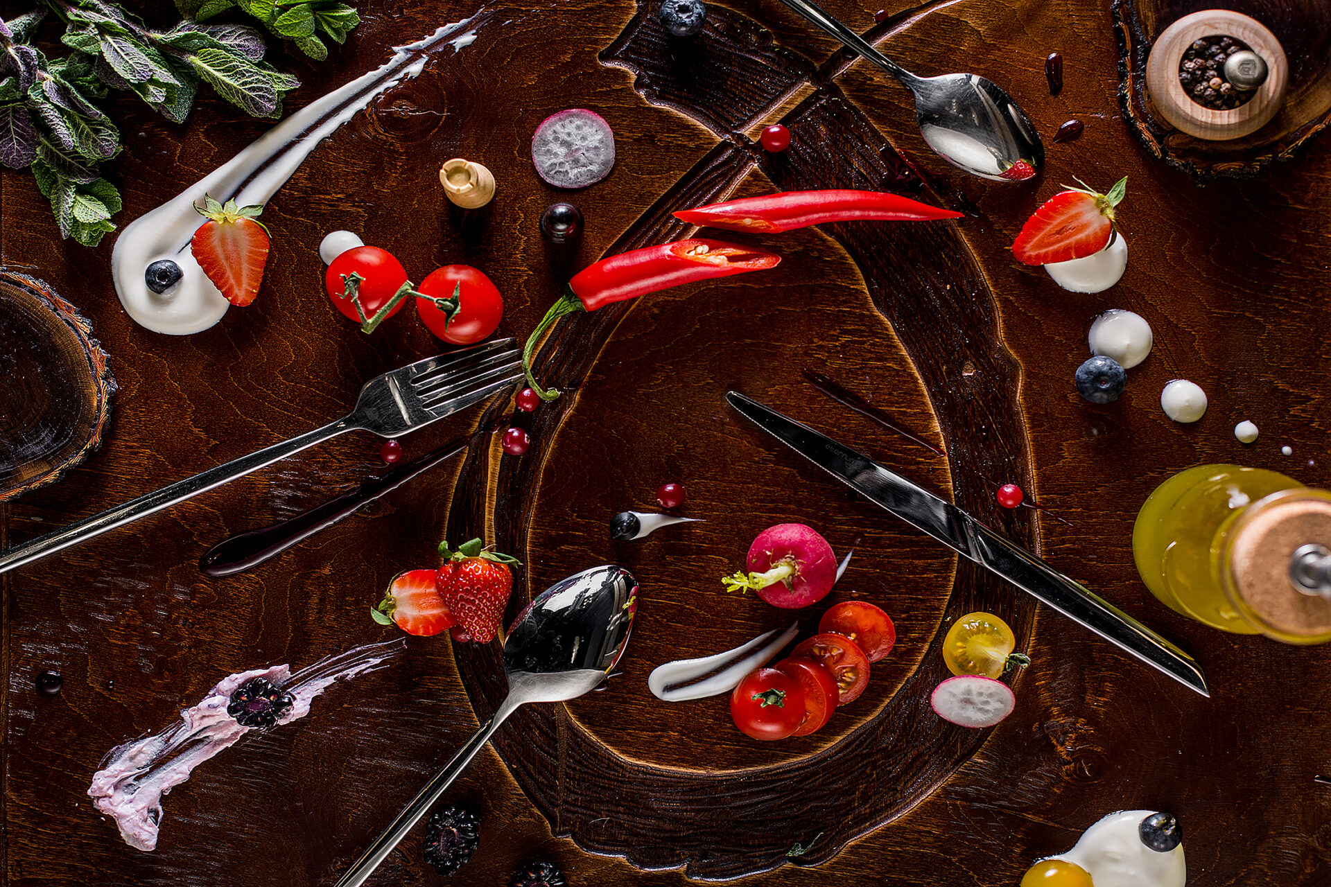 Wooden, lacquered background, with spoons, fork, knife, mint, cherry tomatoes, radishes, strawberries, blueberries, sour cream, peppercorns, blackberries, red currants and olive oil