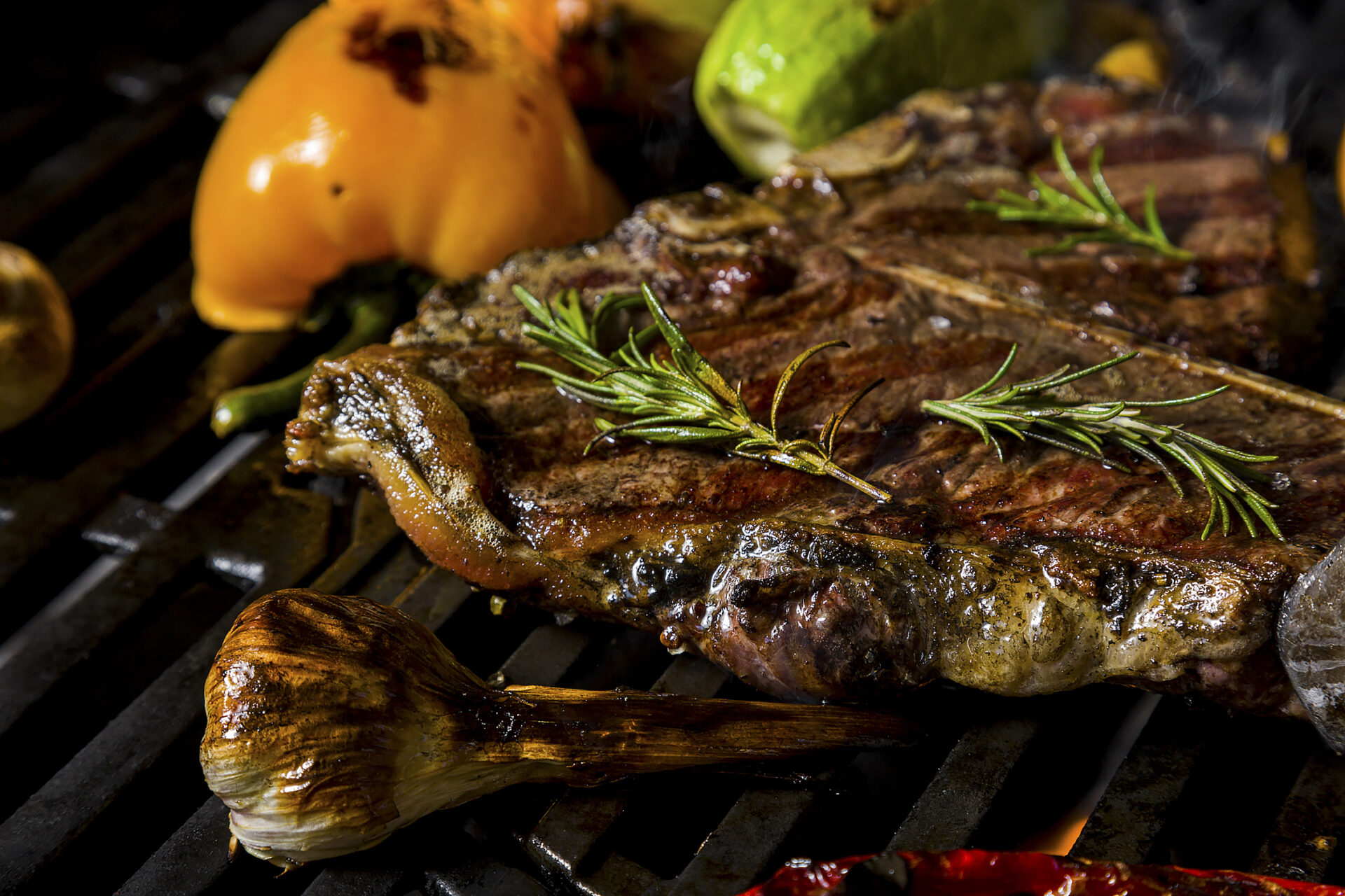 Grilled beef steak on the bone with rosemary, garlic, onion, pepper, zucchini, tomatoes lying on the embers. Horizontal orientation