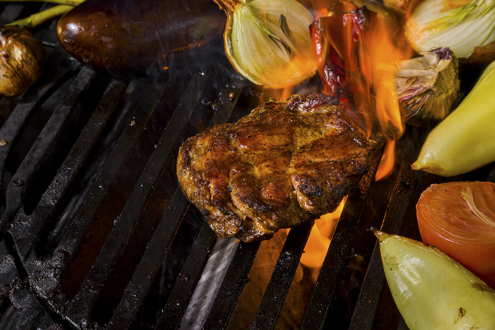 Grilled pork steak with rosemary, garlic, onions, peppers, mushrooms, zucchini, tomatoes on burning coals on fire. Horizontal orientation